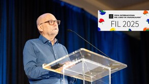 Un hombre de edad, con gafas y camisa de cuadros, habla detrás de un atril de acrílico en un evento. El logo de la FIL (Feria Internacional del Libro) 2025 está