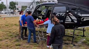 Paramédicos del SAMU Jalisco ingresando una camilla a un helicóptero negro estacionado sobre pasto al exterior de un hospital