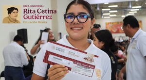 Alumna de secundaria con lentes viendo de frente y sonriendo mientras sostiene un sobre del Banco del Bienestar con personas de fondo
