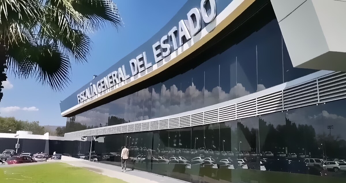 Vista de la fachada exterior de la Fiscalía General del Estado de Michoacán con automóviles estacionados alrededor y una persona caminando