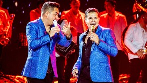 Se ven a dos hombres vestidos con saco azul brillante cantando.