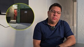 Hombre con playera azul y lentes de contacto y una foto pequeña de una casa