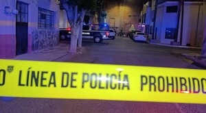 Cinta policiaca amarilla en primer plano y de fondo una patrulla de la Policía Municipal de Guadalajara estacionada detrás de un poste y un árbol