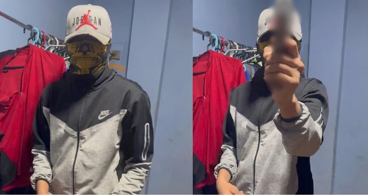 Joven con chamarra nike, gorra y pañoleta sobre el rostro sosteniendo un arma de fuego al lado de un perchero con ropa