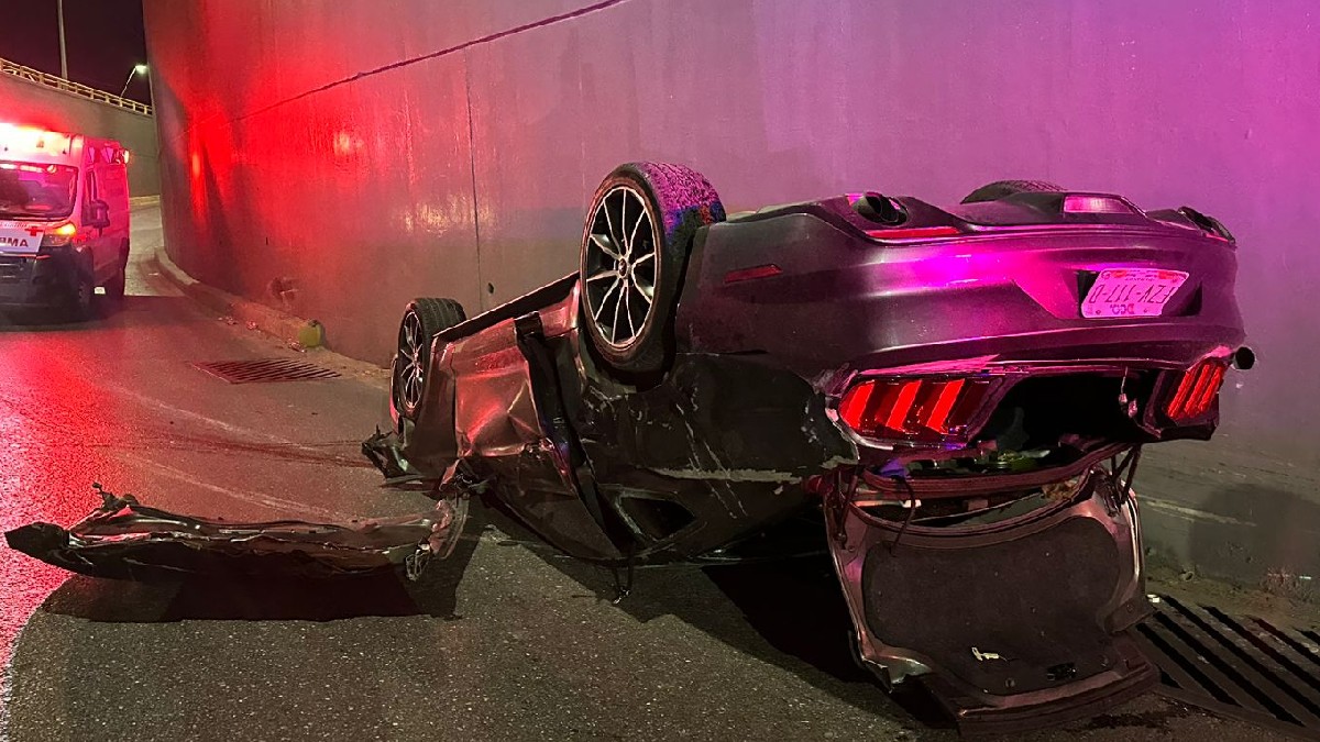 Carro deportivo Mustang color gris volteado tras sufrir aparatoso accidente; autoridades en el lugar.