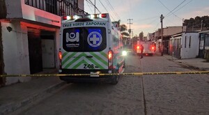 Vista trasera de una ambulancia de la Cruz Verde de Zapopan estacionada al exterior de una casa y detrás de una cinta policial amarilla