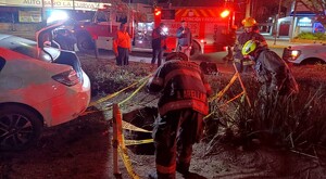 Bomberos de Jalisco alrededor de un socavón acordonado con un automóvil blanco a un costado con la cajuela abierta, personas y un camión de bomberos detrás