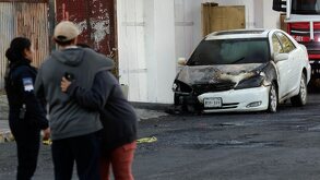Personas llorando frente a un vehículo consumido por un incendio.