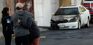 Personas llorando frente a un vehículo consumido por un incendio.