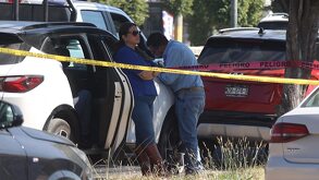 Personas recargadas sobre un vehículo blanco, en medio de una escena acordonada por la policía.