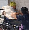 Una mujer anciana en una silla de ruedas platicando con un hombre joven.