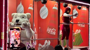 Se observa a una chica vestida de rojo con blanco subida en un carro alegórico, también una botarga de oso blanco.