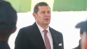 Un hombre vestido de traje y corbata roja realizando una mueca.