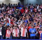 Una gran multitud de aficionados de Chivas (la mayoría vistiendo camisetas de rayas rojas y blancas) animan ruidosamente desde las gradas de un estadio