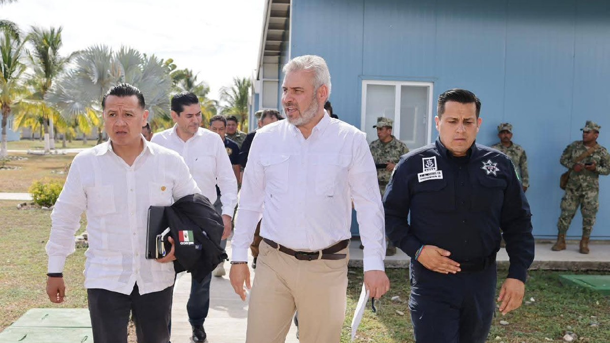 El político Alfredo Ramírez Bedolla (centro, camisa blanca) camina junto a un hombre en un uniforme policial y otros asistentes bajo un sol brillante