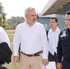 El político Alfredo Ramírez Bedolla (centro, camisa blanca) camina junto a un hombre en un uniforme policial y otros asistentes bajo un sol brillante