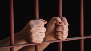 Se observan unas manos de una mujer agarrando barrotes de una cárcel.