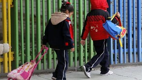 Niños abrigados entrando a una escuela con sus uniformes y mochilas.