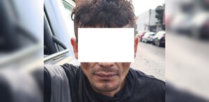 Hombre detenido viendo de frente con los ojos censurados, vistiendo una playera negra con una calle de fondo y automóviles estacionados a los costados