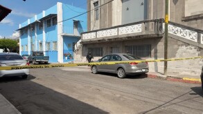Vista sobre la batea de una camioneta de POLICÍA ESTATAL en la calle de una ciudad colonial (Colima). La calle está acordonada con cinta amarilla, y se ven edif