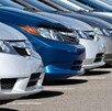 Una fila de autos modernos estacionados de frente, incluyendo modelos en color plateado, blanco y un prominente coche azul brillante en el centro. La foto está