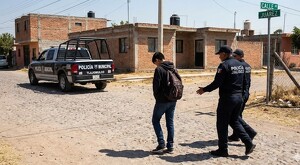 Adolescente visto de espaldas caminando con su mochila mientras es llevado por policías de Jalisco hasta una patrulla de la Policía de Tlajomulco