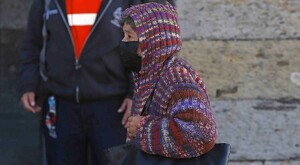 Mujer mayor vistiendo un abrigo tejido y un cubrebocas mientras sostiene una bolsa negra al hombro caminando por calles de Guadalajara
