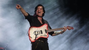 Saúl Hernández, vocalista de la banda Caifanes, sosteniendo una guitarra arriba de un escenario.