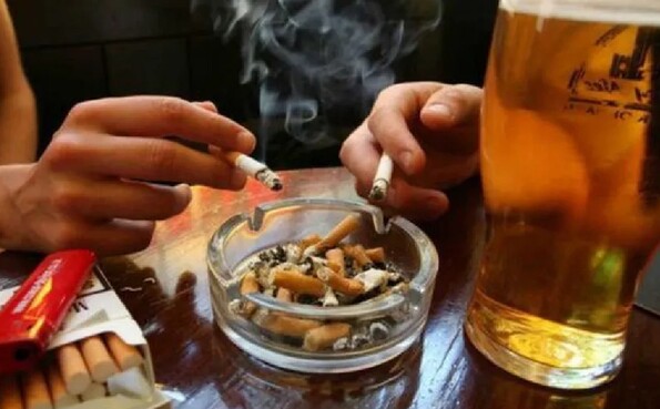 Colillas de cigarros y dos vasos de vidrios con cerveza