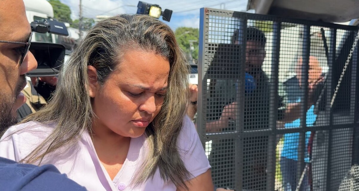 Gleyza Vasconcelos de Oliveira viendo hacia abajo mientras es detenida por policías de Brasil con periodistas en el fondo