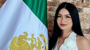 Una mujer de cabello negro posando junto a una bandera de México.