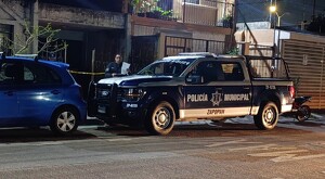 Patrulla de la Policía Municipal de Zapopan estacionada frente a casas con un automóvil azul al frente y un oficial con documentos a un costado