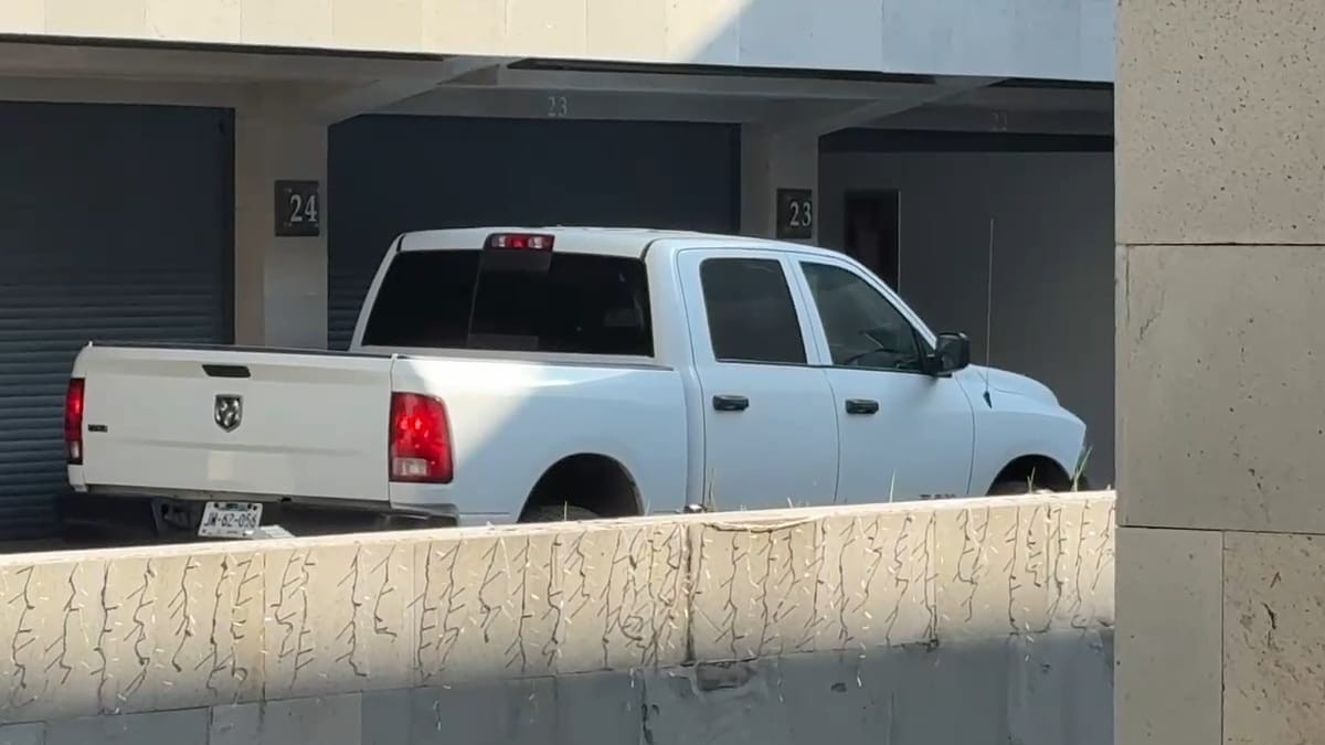 Una camioneta blanca de cuatro puertas (marca Dodge Ram) está estacionada parcialmente en una cochera numerada (el número 23 es visible).