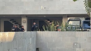 Agentes de policía (uniforme oscuro) están de pie dentro de la entrada de un motel con el número 15 en la pared, cerca de una escalera. Un vehículo 4x4 abierto