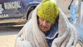 Una mujer de la tercera edad cubierta con un gorro y en silla de ruedas.