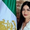 Una mujer de cabello negro posando junto a una bandera de México.