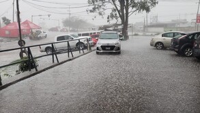 Una capa gruesa de granizo cubre completamente el piso de un estacionamiento abierto. Varios autos están estacionados y una camioneta blanca está a la izquierda