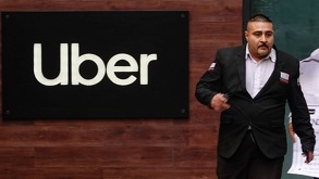 Un hombre de traje caminando con un logo de Uber de fondo.