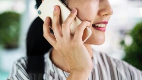 Primer plano lateral de una mujer sosteniendo un teléfono inteligente dorado en su oreja, sonriendo ligeramente. Lleva una blusa de rayas y tiene las uñas corta
