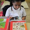 Se observa a una niña con un libro dentro de un salón de clases.