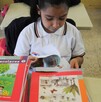 Se observa a una niña con un libro dentro de un salón de clases.