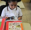 Se observa a una niña con un libro dentro de un salón de clases.