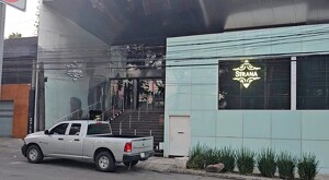 Vista exterior del antro Strana con las paredes quemadas, una camioneta estacionada en frente y unas plantas sembradas en la banqueta