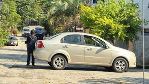 Un policía parado junto a un vehículo estacionado, mirando de lejos una escena del crimen.