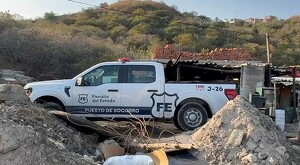 Camioneta blanca de la Fiscalía del Estado de Jalisco en medio de un predio con diversos escombros frente a un pastizal