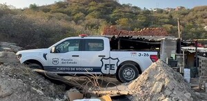 Camioneta blanca de la Fiscalía del Estado de Jalisco en medio de un predio con diversos escombros frente a un pastizal