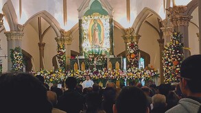 Se observa un sacerdote y frente a él muchas personas dentro de una iglesia.