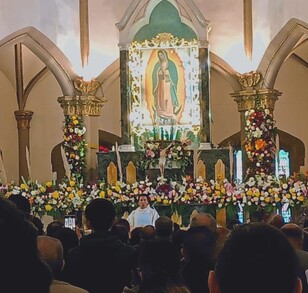 Se observa un sacerdote y frente a él muchas personas dentro de una iglesia.