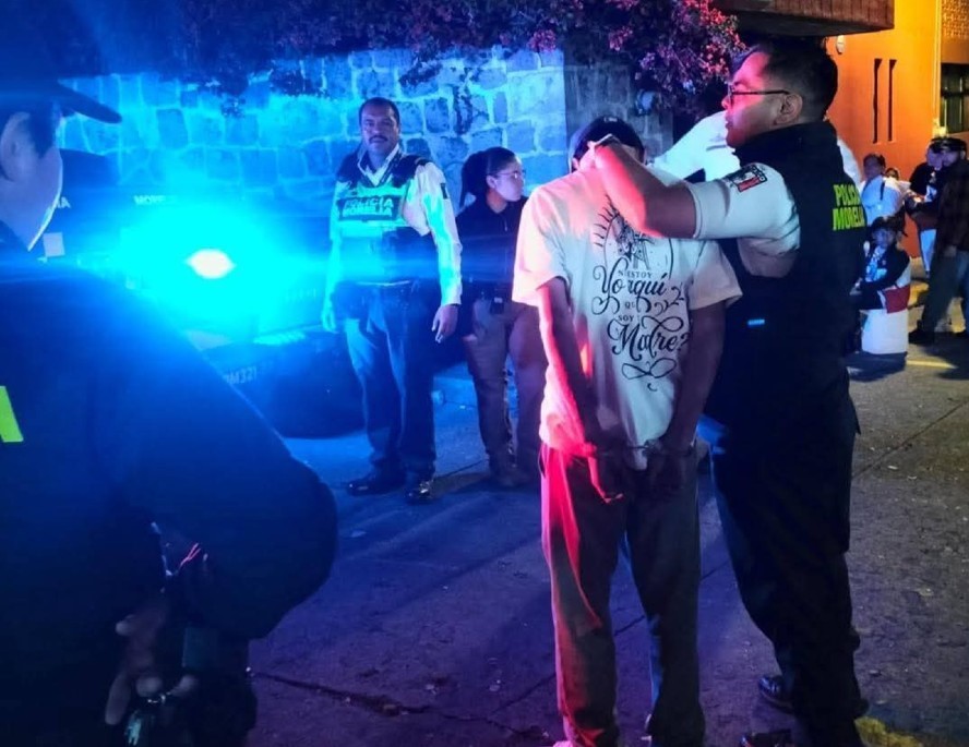 Oficial de Morelia sujetando a un hombre con las manos esposadas en la espalda y otros elementos de la policía alrededor