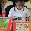 Se observa a una niña con un libro dentro de un salón de clases.